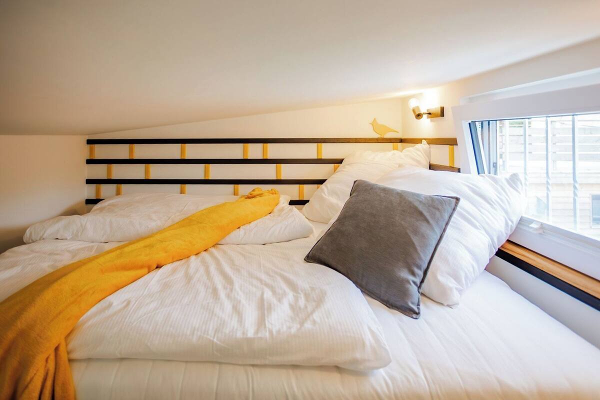 A neatly made bed with white linens, a yellow throw blanket, and a gray pillow.