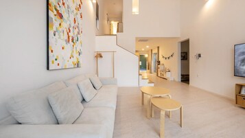 Uma sala de estar moderna com um sofá, uma mesa de centro e uma escada que dá para uma cozinha.