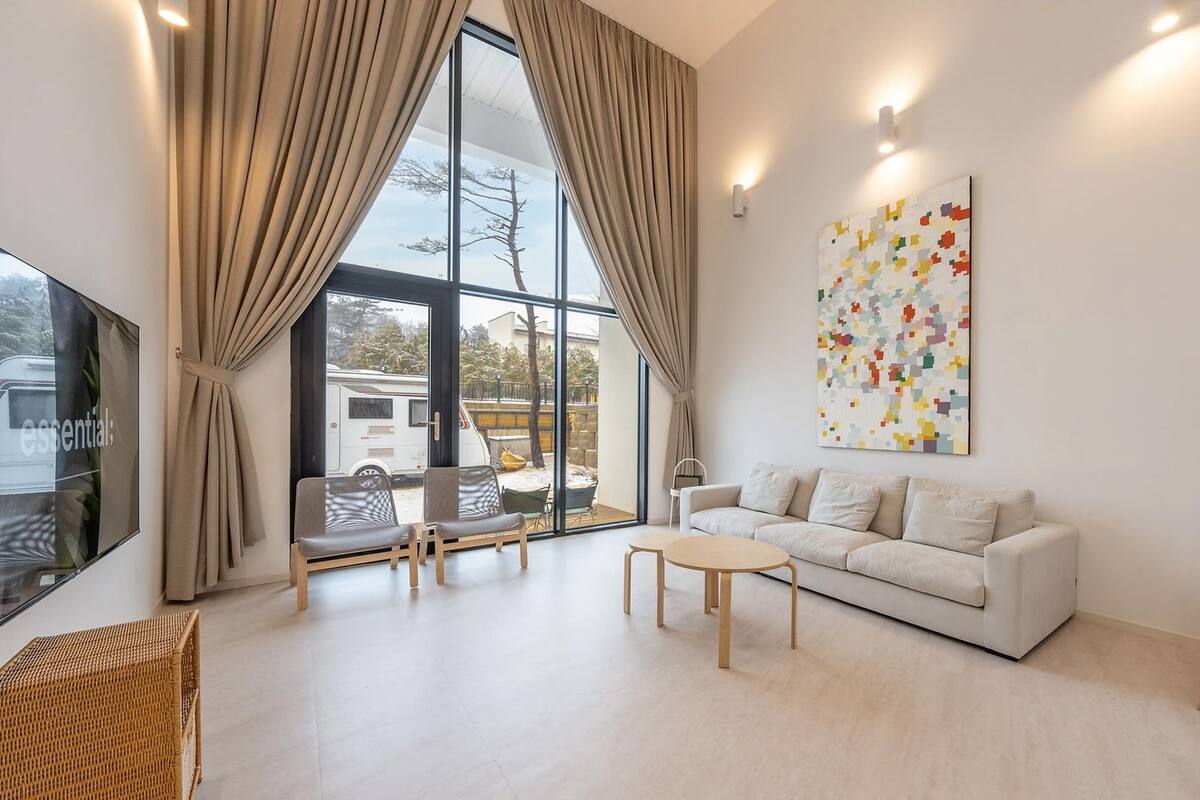 A modern living room with a large window, a sofa, a coffee table, and a colorful abstract painting.