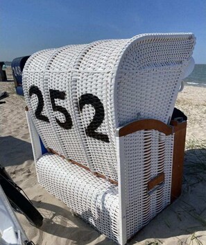 Une chaise en osier blanche, portant le numéro 252 sur son dossier, est placée sur une plage de sable.
