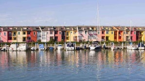 A row of colorful row houses by a calm waterfront with boats docked in front. - Gorgeous Caorle resort near the beach (Caorle (VE))