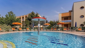 A swimming pool with a water fountain, surrounded by lounge chairs and umbrellas, with a building in the background. - Gorgeous Caorle resort near the beach (Caorle (VE))