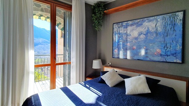 Ein Schlafzimmer mit einem großen Bett, einem Gemälde an der Wand, einem Balkon mit Blick und einem Fenster mit Vorhängen.