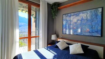 Ein Schlafzimmer mit einem großen Bett, einem Gemälde an der Wand, einem Balkon mit Blick und einem Fenster mit Vorhängen.