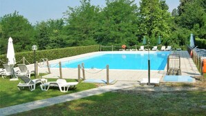 Ein rechteckiger Swimmingpool mit glasklar blauem Wasser, umgeben von einer niedrigen Hecke, ausgestattet mit Liegestühlen und Sonnenschirmen.