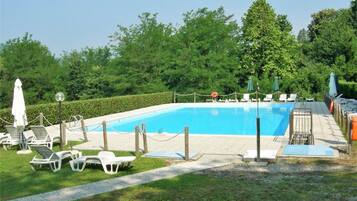 Ein rechteckiger Swimmingpool mit glasklar blauem Wasser, umgeben von einer niedrigen Hecke, ausgestattet mit Liegestühlen und Sonnenschirmen.