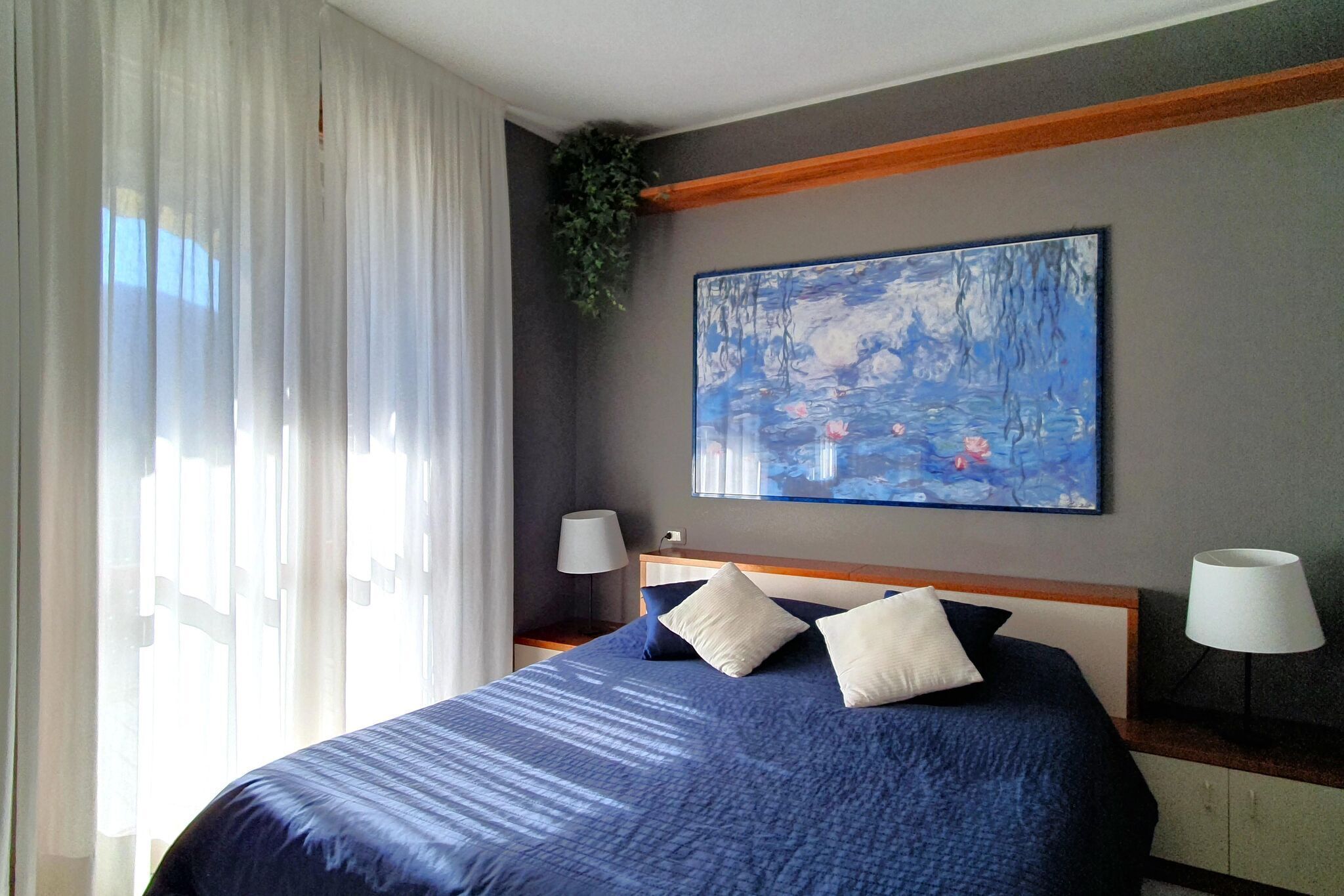 Ein Hotelzimmer mit einem großen Bett, zwei Nachttischlampen, einem Bild an der Wand und transparenten Vorhängen.