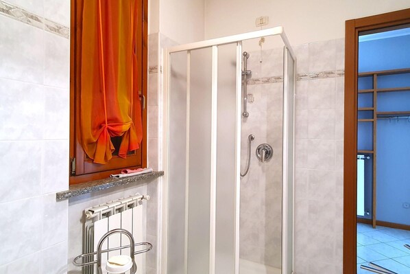 Un baño con ducha acristalada, un perchero y un radiador.