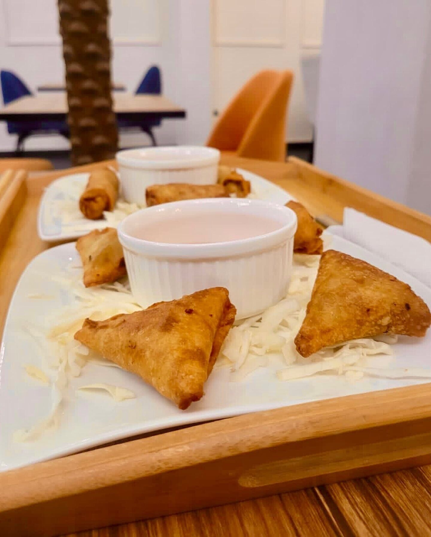 A tray with samosas and a dipping sauce on a wooden table.