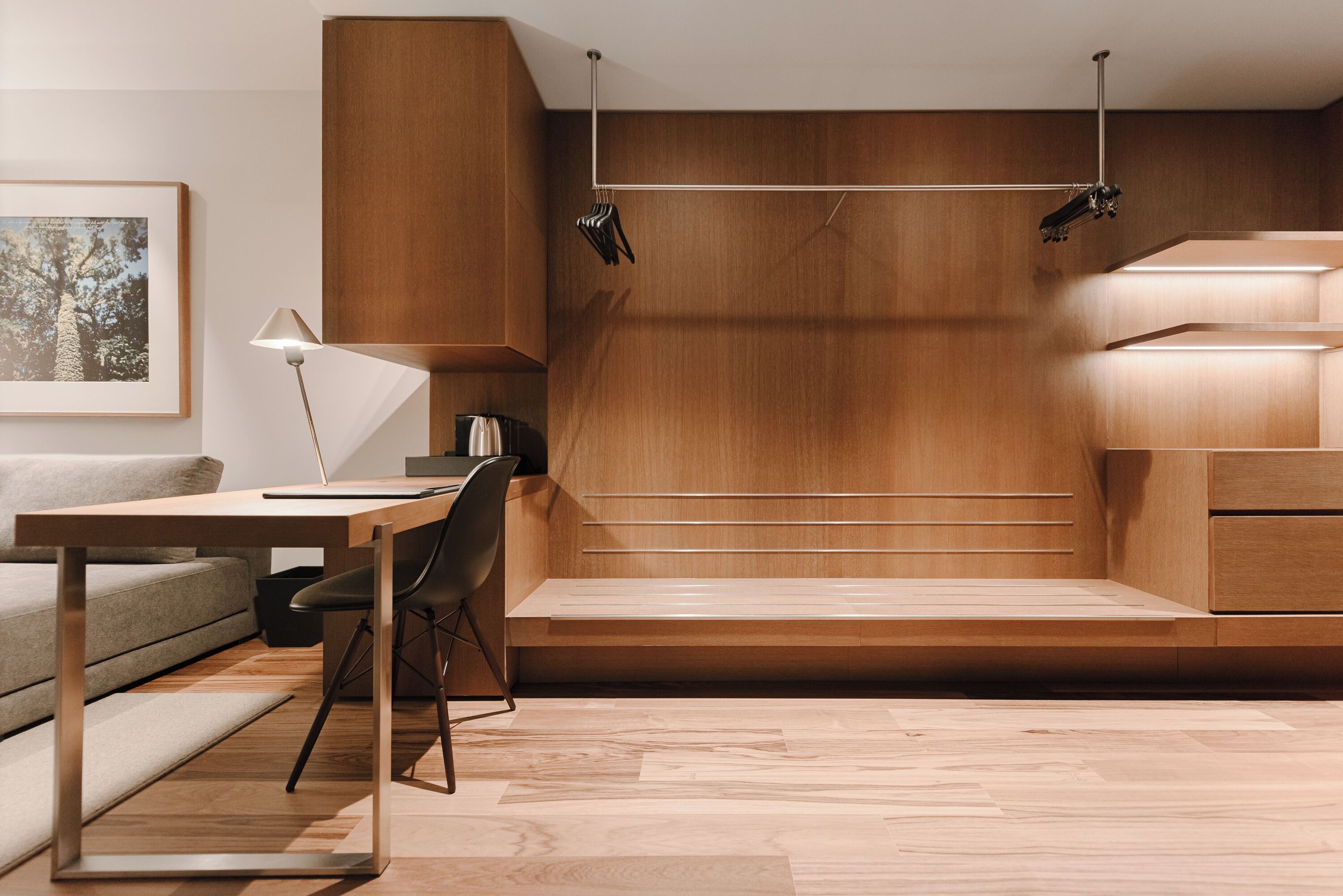 A modern room with a wooden desk, a chair, a sofa, and a framed picture on the wall.