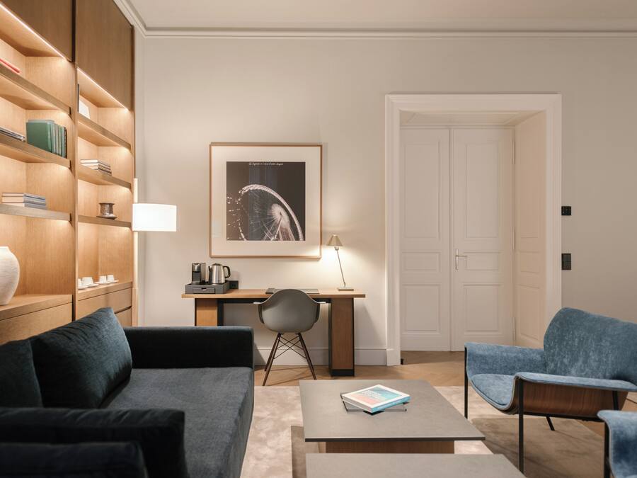 A modern living room with a sofa, two armchairs, a coffee table, a desk with a chair, a bookshelf, and a framed picture on the wall.