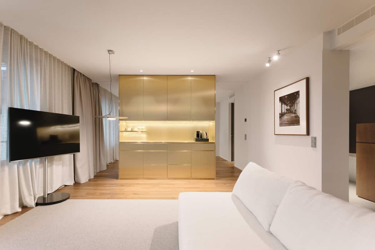 A modern living room with a flat-screen TV, a white sofa, and a kitchen area in the background.