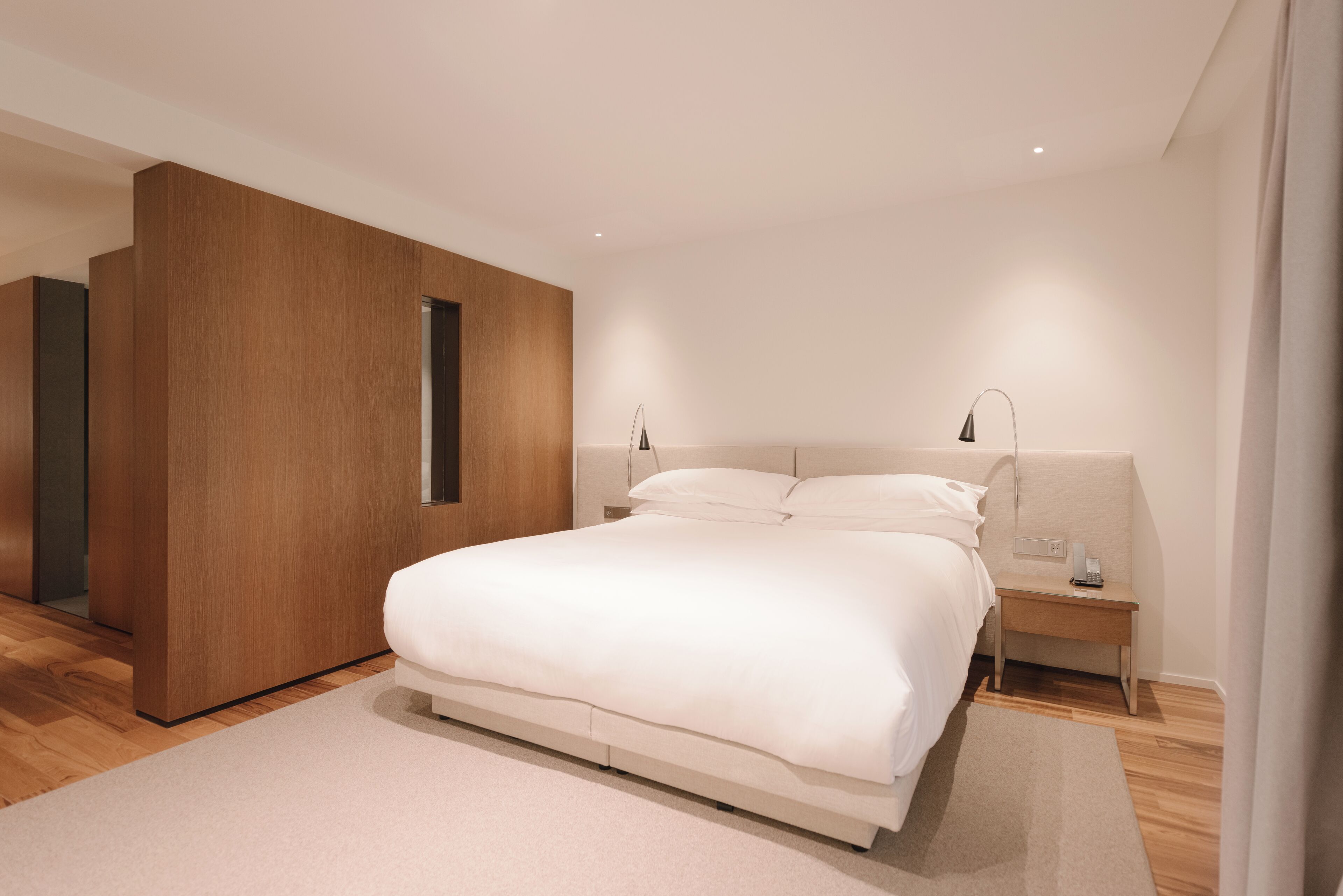 A modern bedroom with a large bed, wooden paneling, and bedside lamps.