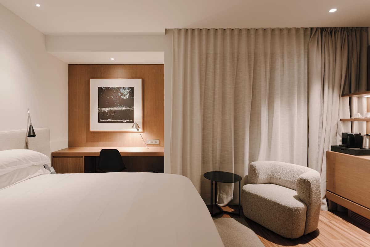 A hotel room with a large bed, a desk with a chair, a small round table, a sofa, and a wooden dresser.
