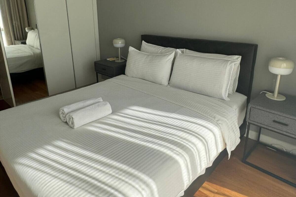Un lit bien fait, avec du linge de lit blanc et des oreillers, une table de chevet avec une lampe et un miroir au mur.