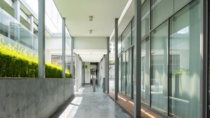 A modern building corridor with glass walls, a concrete planter with greenery, and a tiled floor. - The Signature - Serviced residence (Kuala Lumpur)