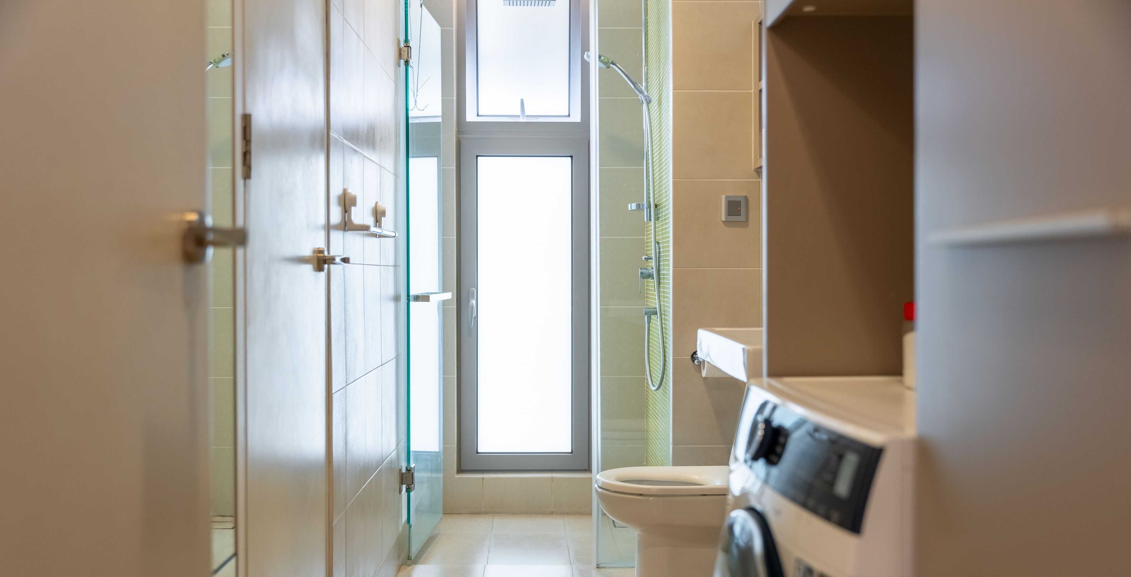 A modern bathroom with a glass shower enclosure, a toilet, and a washing machine.