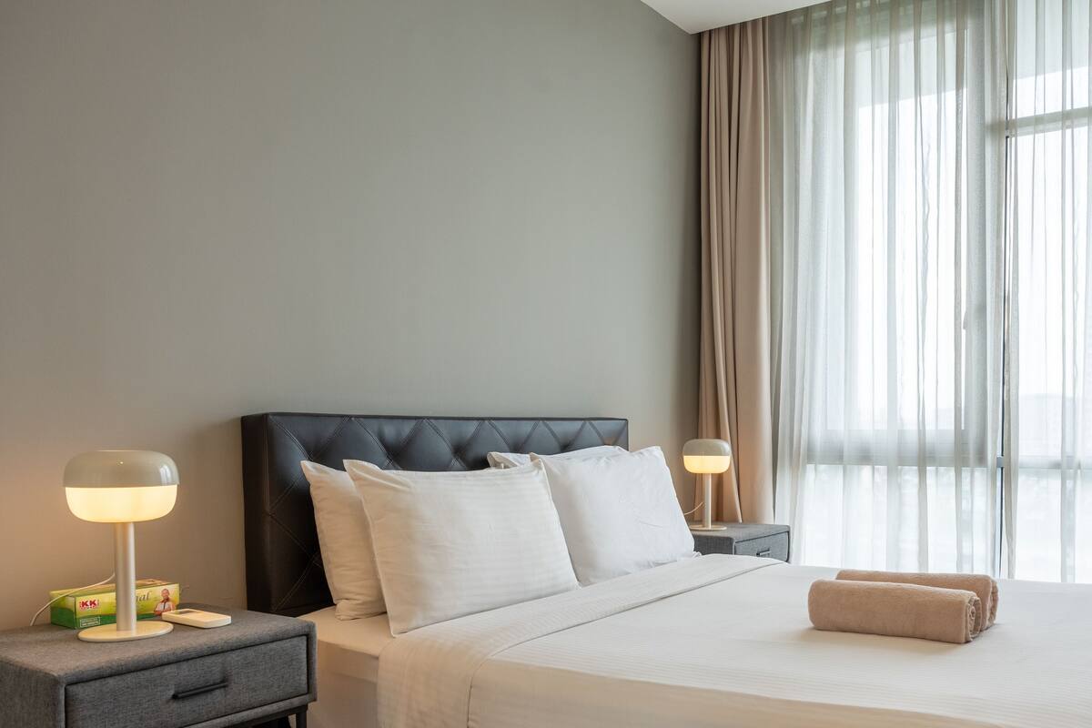 Une chambre d’hôtel avec un lit, deux tables de chevet, une lampe et une fenêtre avec des rideaux.