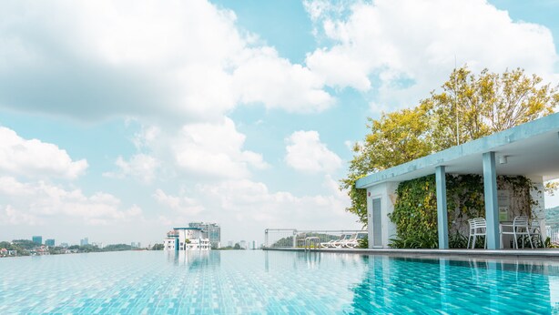 A pool with clear blue water, a covered seating area with chairs, and a view of a cityscape in the background. - The Signature - Serviced residence (Kuala Lumpur)