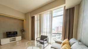 A modern living room with a flat-screen TV, a glass coffee table, a grey sofa, and a view of a cityscape through large windows. - The Signature - Serviced residence (Kuala Lumpur)