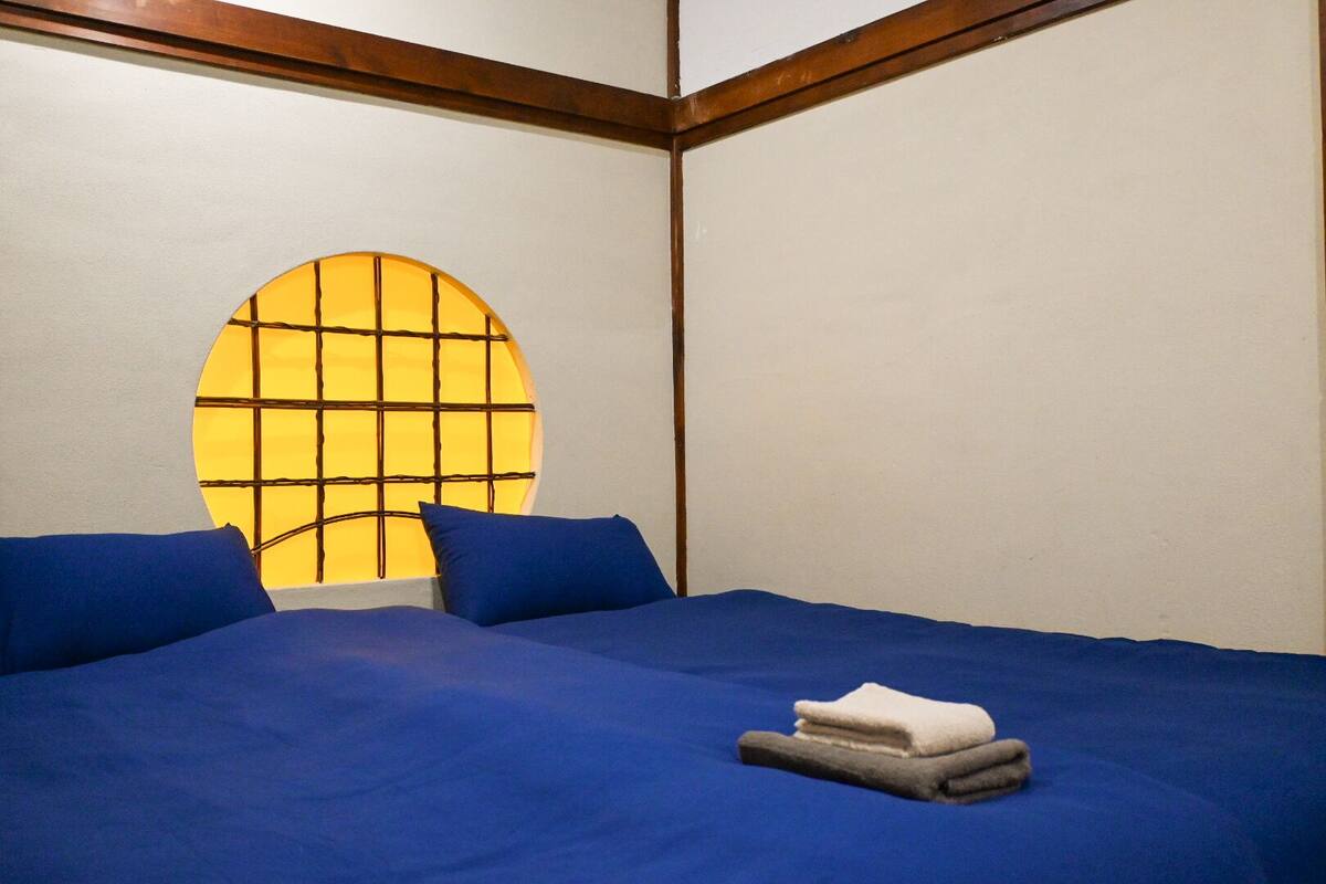 A room with a bed, two pillows, a window with a grid pattern, and a wooden beam ceiling.