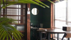Una habitación con un espejo redondo, una mesa, sillas y una ventana con persianas.