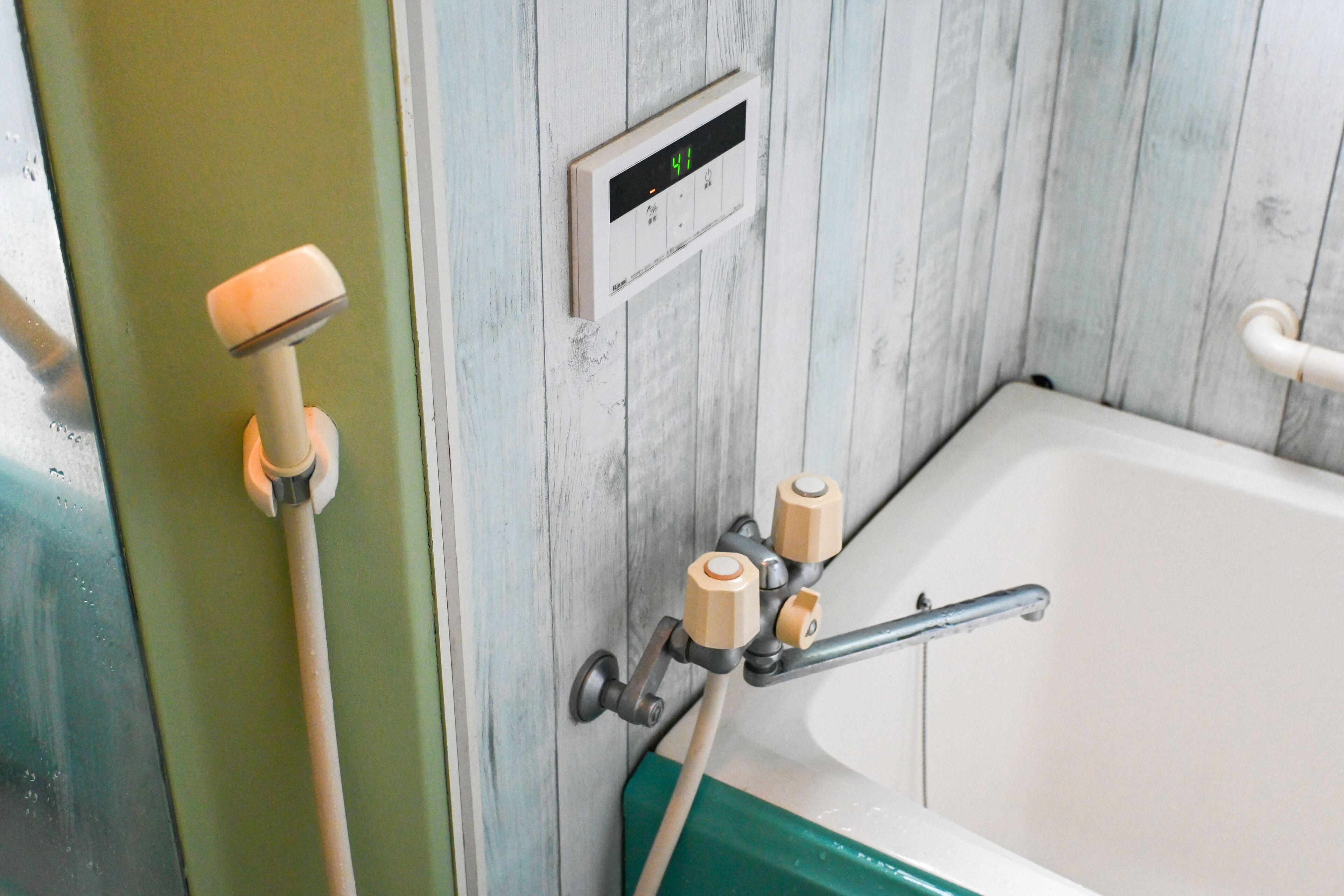 Un baño con pared de paneles de madera, un termostato digital y una bañera con detalle verde.