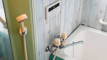 Un baño con pared de paneles de madera, un termostato digital y una bañera con detalle verde.