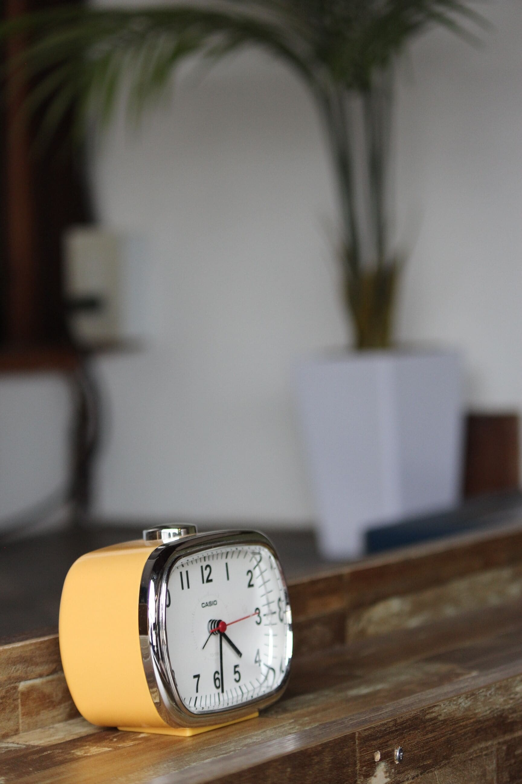 A yellow Casio alarm clock on a wooden ledge with a blurred background.