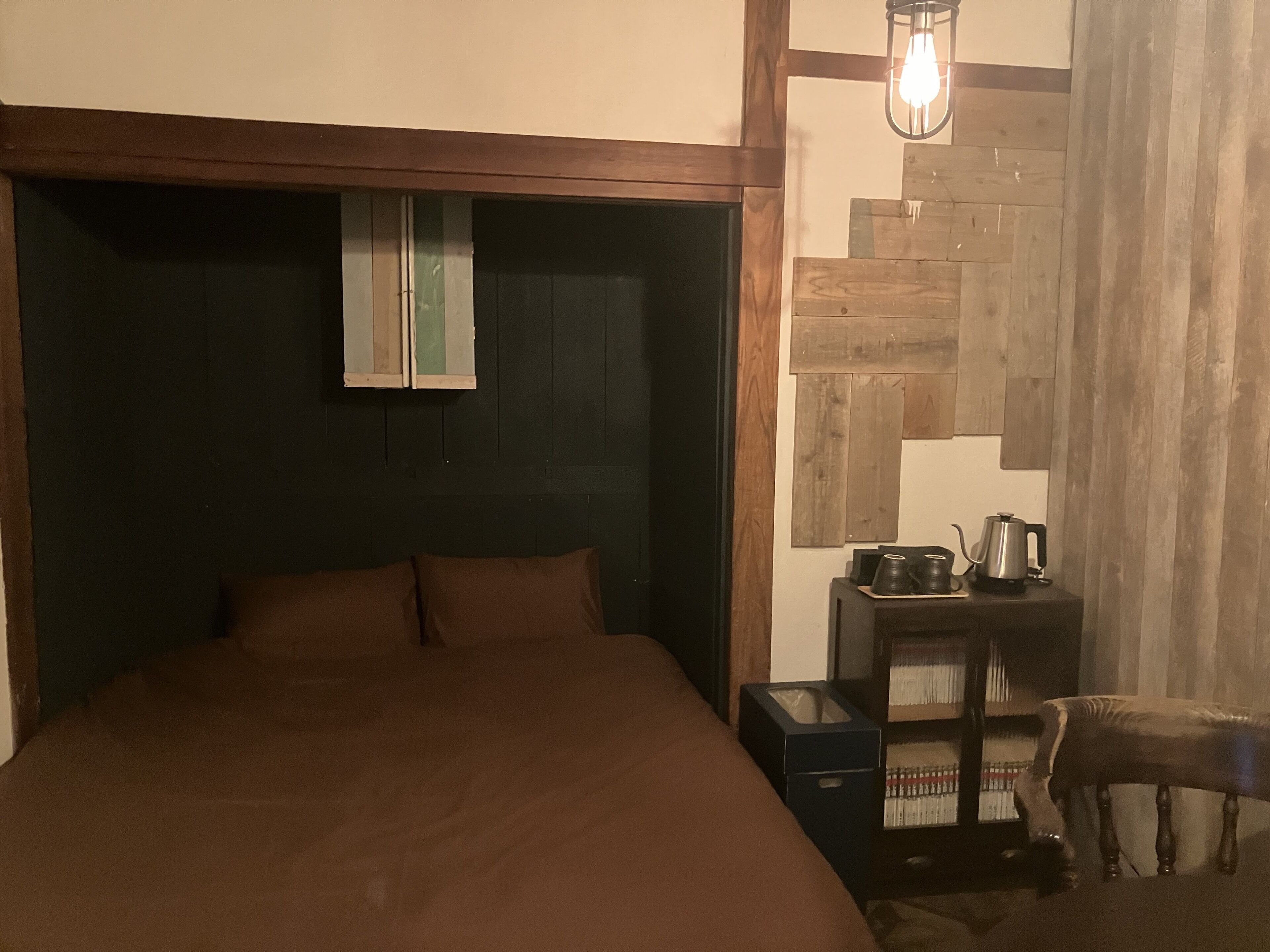 Un dormitorio con una cama grande, una mesita de noche con hervidor y una silla.