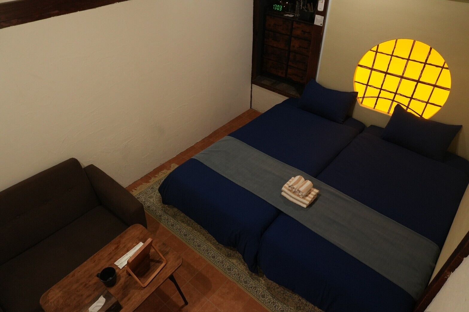 Un dormitorio con cama, una mesita y una ventana con un reloj.