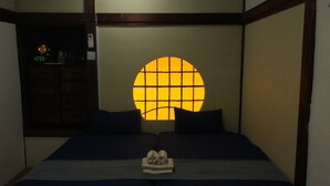 Una habitación tradicional japonesa con suelo de tatami, futón y fusuma con ventanal circular.