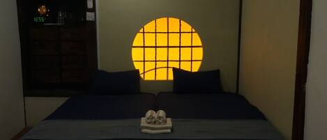 Una habitación tradicional japonesa con suelo de tatami, futón y fusuma con ventanal circular.