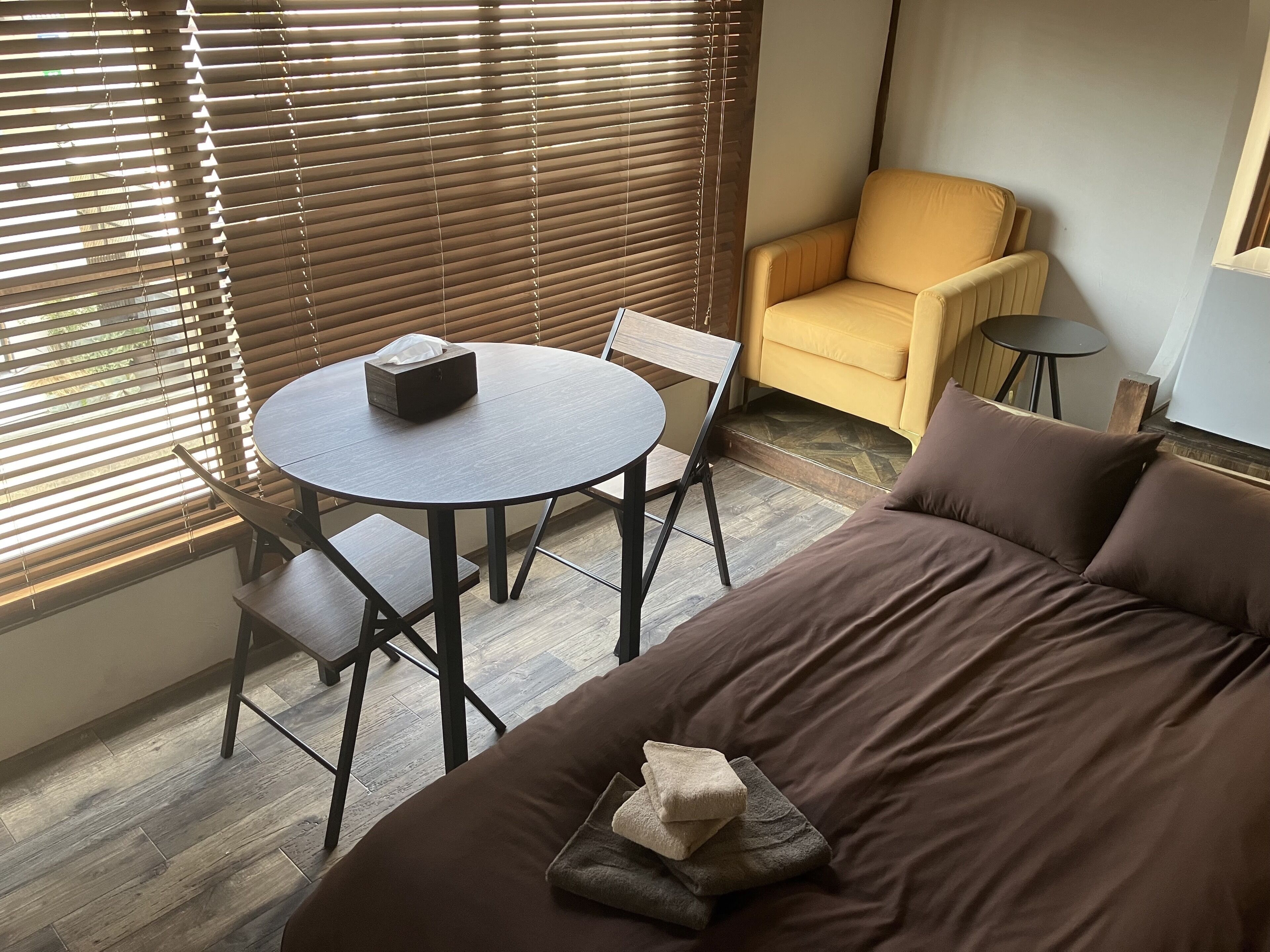 Ein Zimmer mit einem Bett, einem runden Tisch mit Stühlen, einem gelben Sessel und einem kleinen Tisch mit einer Lampe.