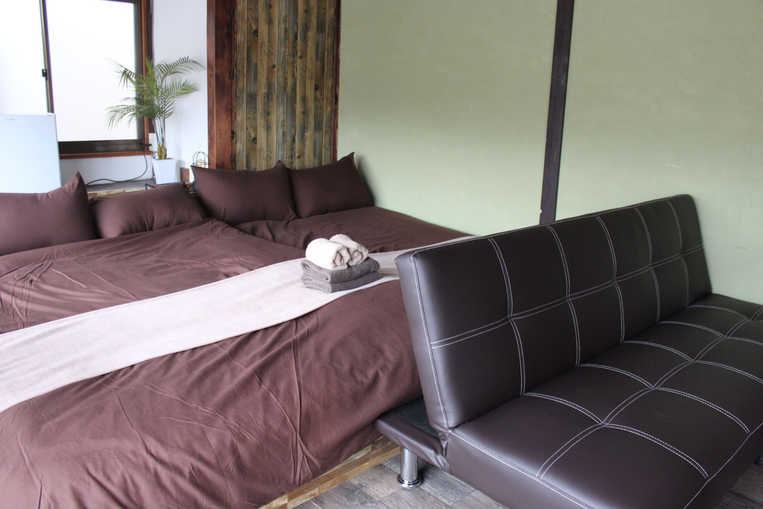 A bedroom with a large bed, a sofa, a plant, and a wooden wall panel.