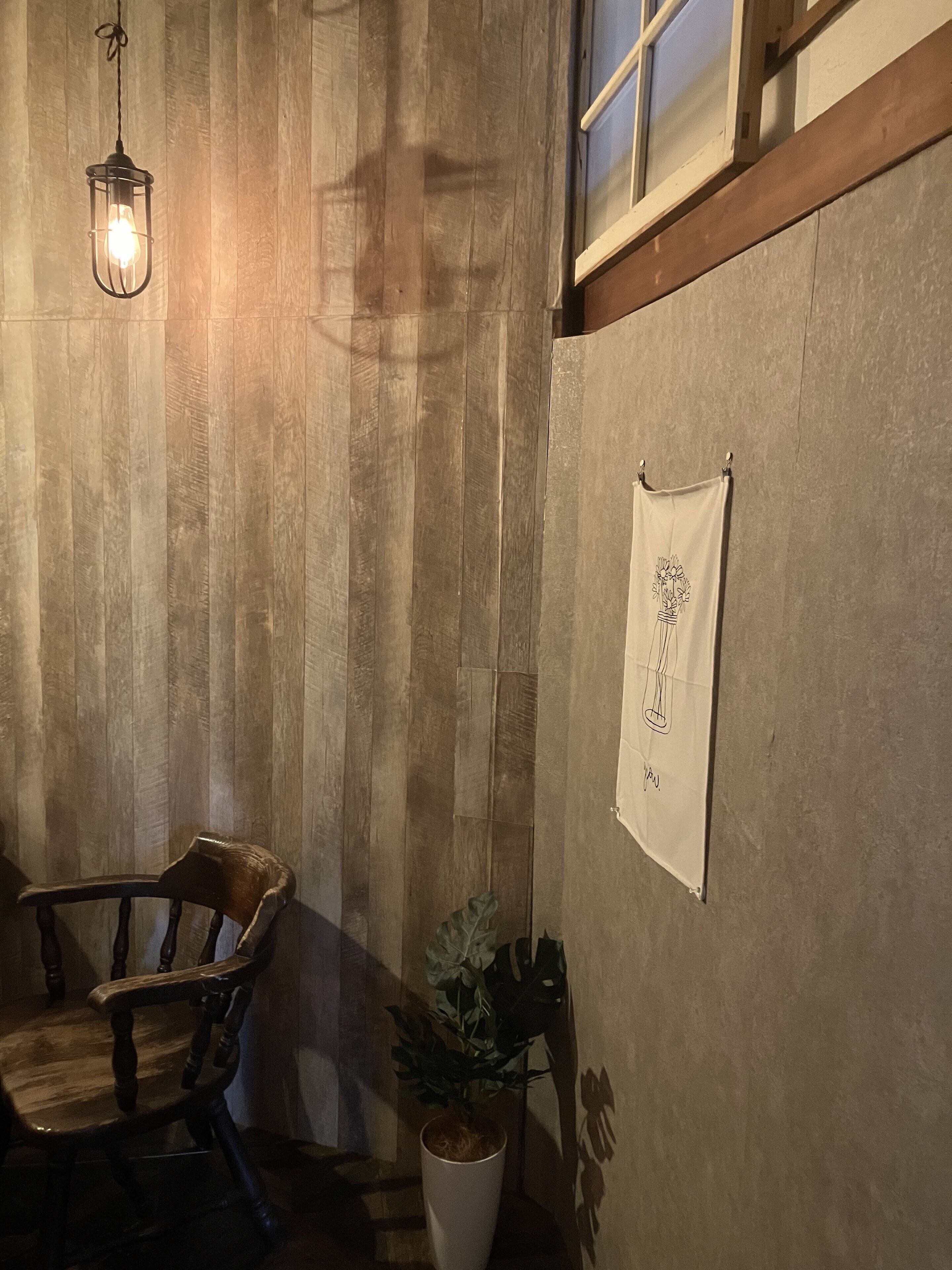 Un interior de madera con una lámpara colgante, una silla de madera, una planta en maceta y un tapiz colgado en la pared.