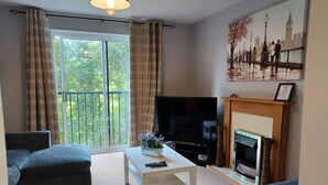 Un salon avec une télévision, une cheminée et un balcon agrémenté de rideaux.