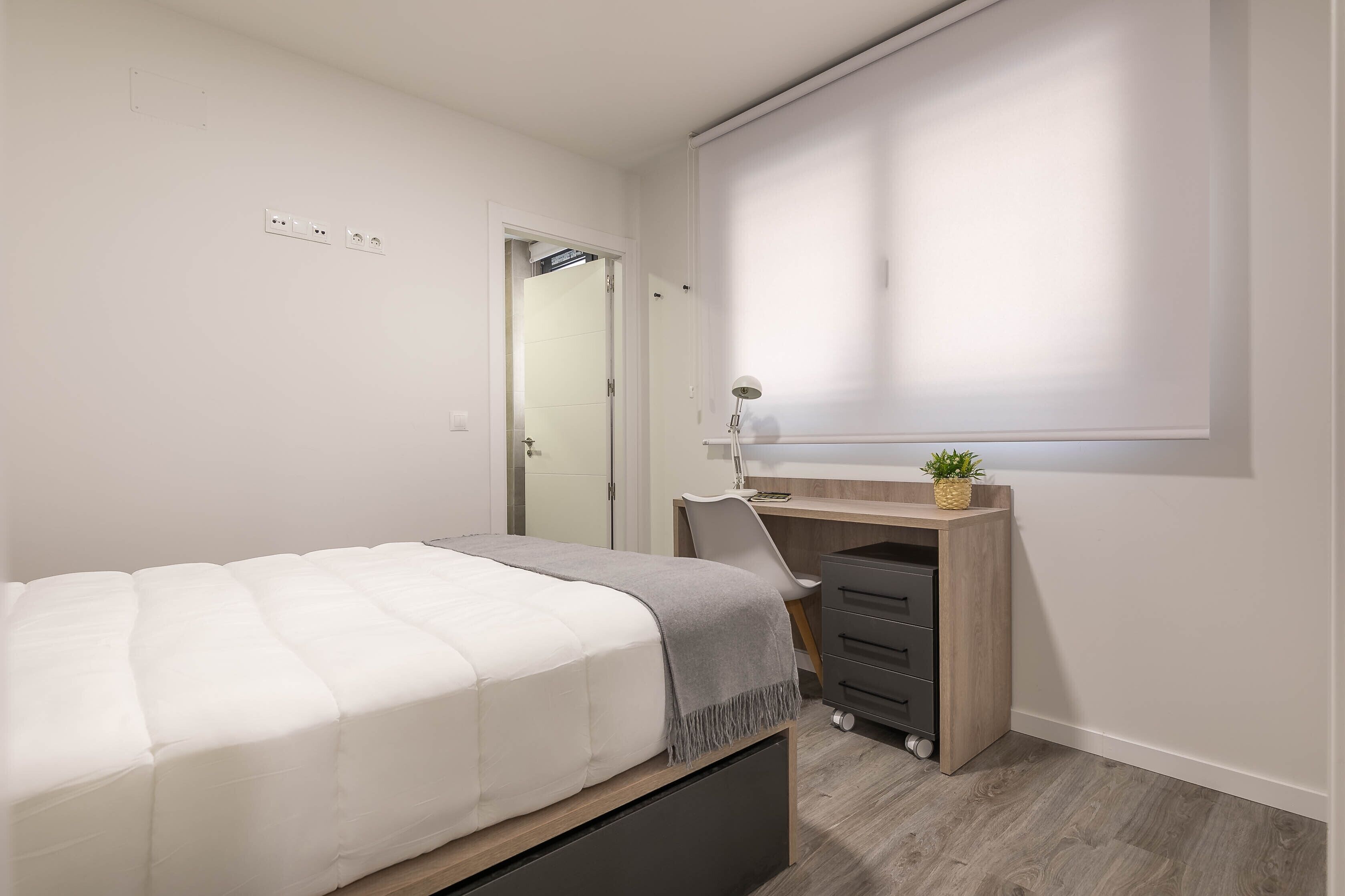 Un dormitorio con cama, escritorio y ventana con persianas.