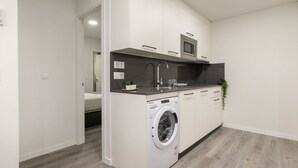Une cuisine compacte équipée d’un lave-linge et d’un sèche-linge intégrés, d’un four à micro-ondes et d’un petit plan de travail.