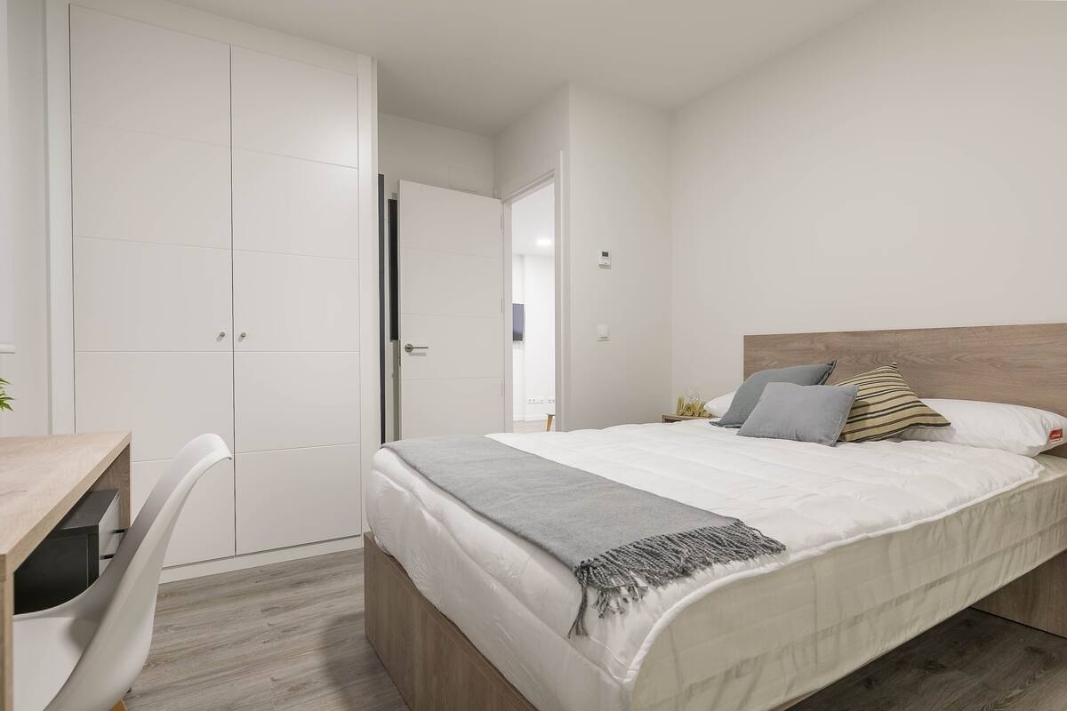 A bedroom with a bed, a desk, and a wardrobe.