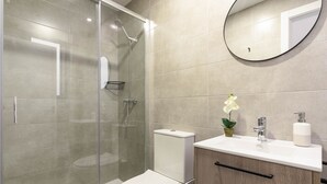 Une salle de bain moderne avec une douche en verre, des toilettes, un lavabo avec un miroir et une petite orchidée en pot.