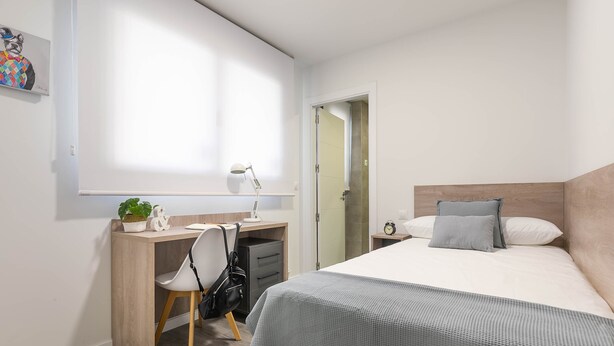Une chambre à coucher comprenant un lit, un bureau, une chaise, une table de chevet et une lampe fixée au mur.