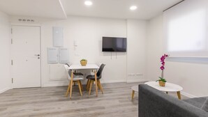 Une pièce moderne et minimaliste comprenant un coin repas, un téléviseur à écran plat fixé au mur et une petite table sur laquelle est posée une orchidée en pot.
