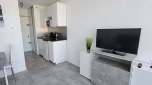 A compact living space with a kitchenette, a dining area, and a television mounted on a wall. - Studio Proche Centre ET Plage Avec Clim ET Parking (La Grande-Motte)