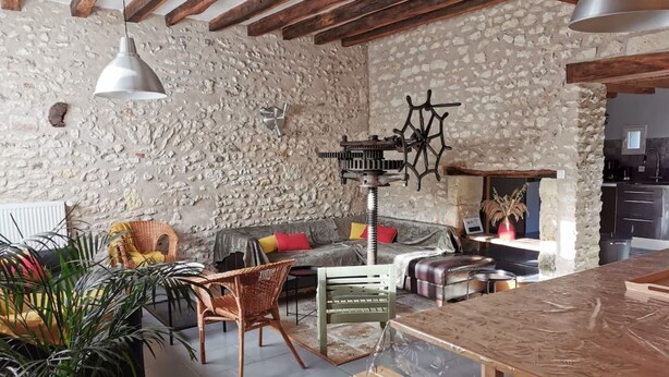 Ein rustikales Interieur mit freiliegenden Steinwänden, Holzbalken, einer Essecke mit Holztisch sowie einer Sitzecke mit Sofa und Sesseln.