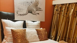 A bedroom with a bed, pillows, a blanket, and a leopard print pillow. - WG Guest Villas  (Bulawayo)