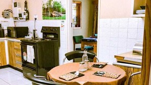 A small, cozy kitchen with a dining area. It includes a stove, a sink, and a refrigerator. There are two chairs around a table with a tablecloth. - WG Guest Villas  (Bulawayo)