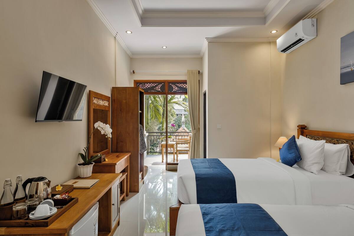 A hotel room with a bed, a desk, a TV, and a balcony with a view of greenery.