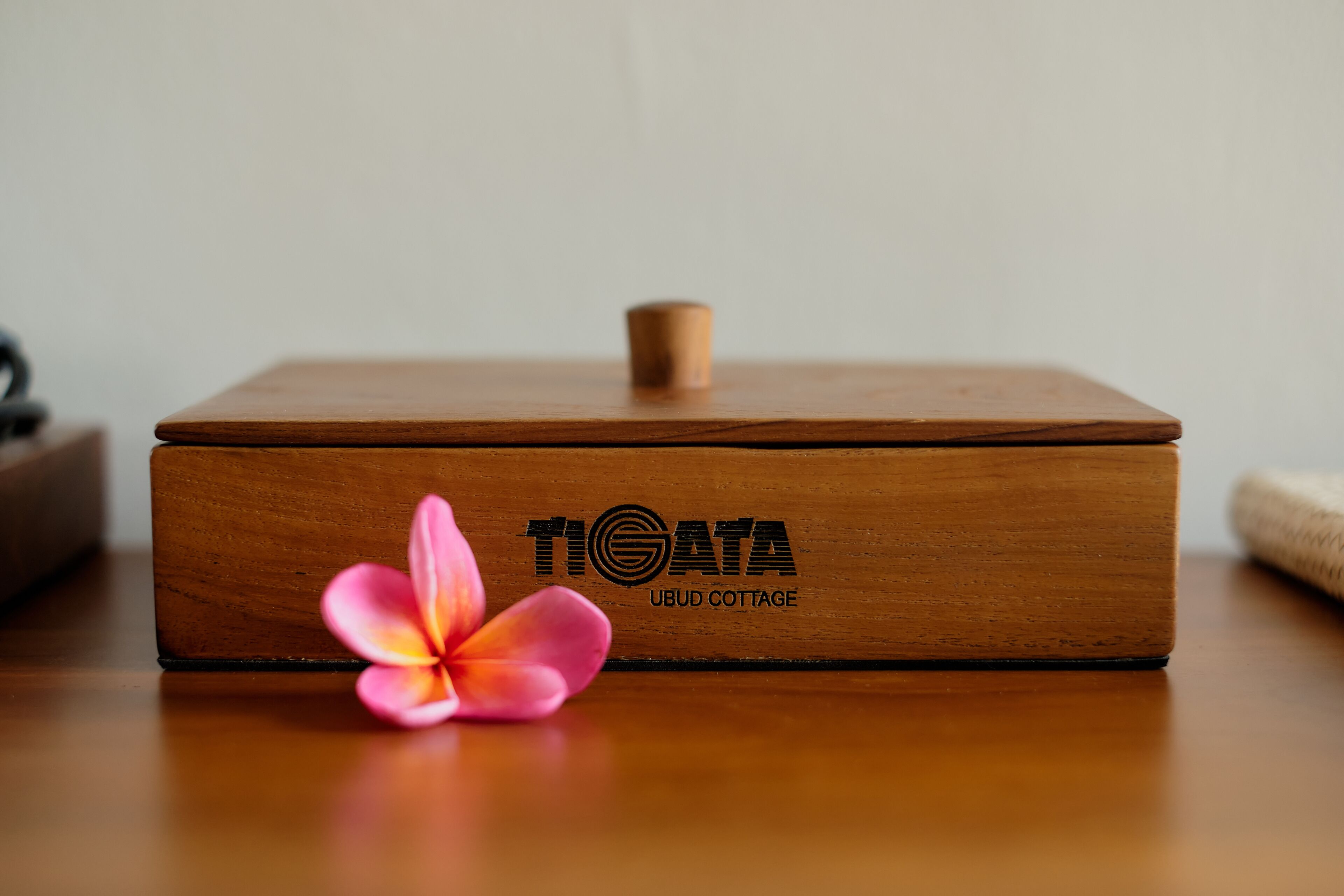 A wooden box with the text "TIGATA UBUD COTTAGE" on it, placed on a wooden surface.