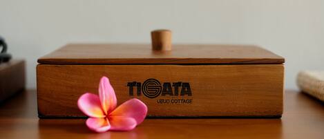 Una scatola di legno con la scritta "TIGATA UBUD COTTAGE", appoggiata su una superficie in legno.